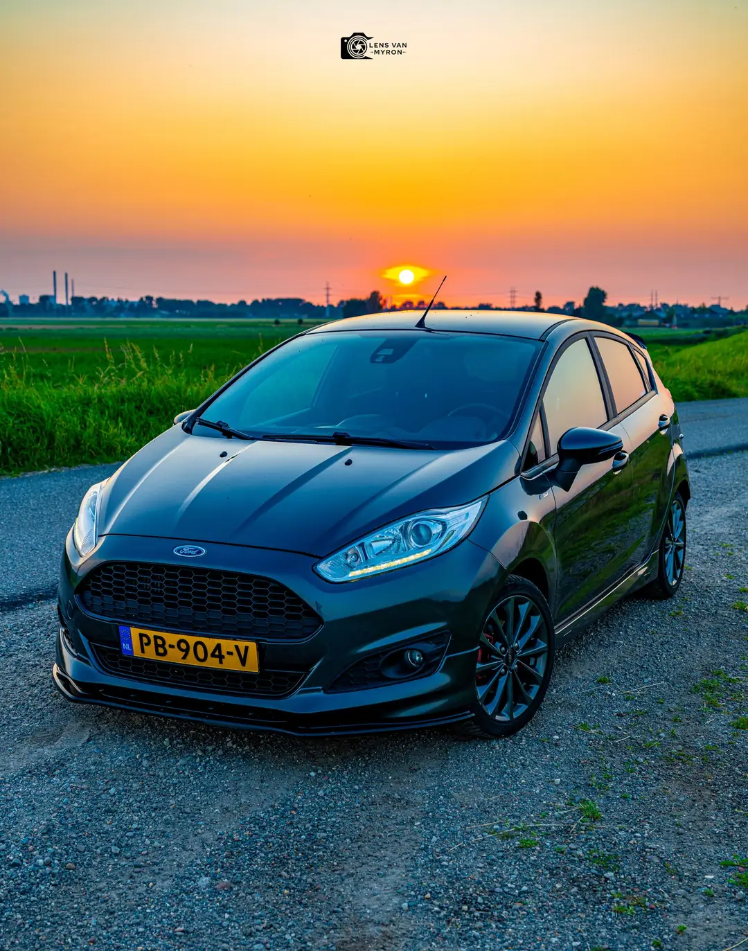 Ford Fiesta van voren op een grindpad met de ondergaande zon boven de horizon en een oranje lucht