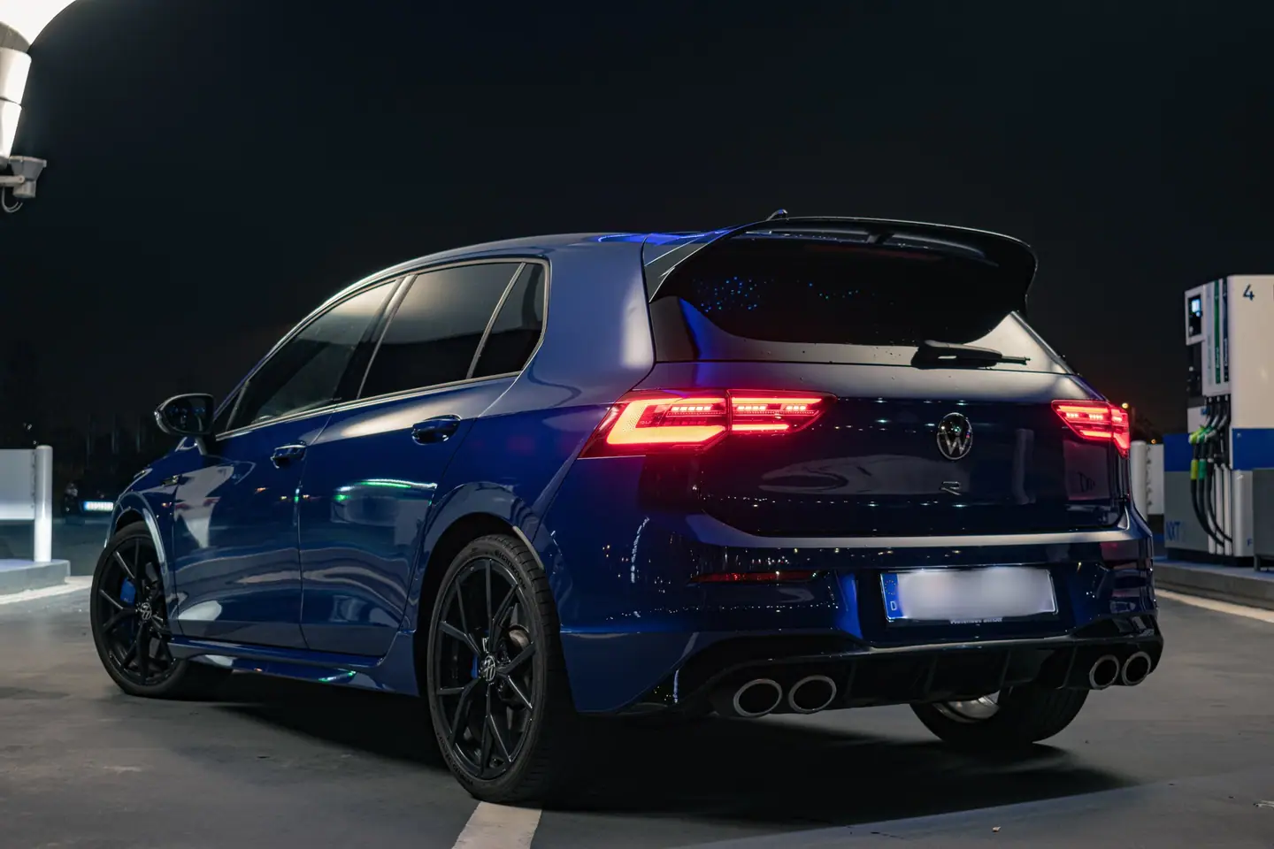 Blauwe Volkswagen Golf R schuin van achteren bij nacht op een tankstation, met fel rode achterlichten
