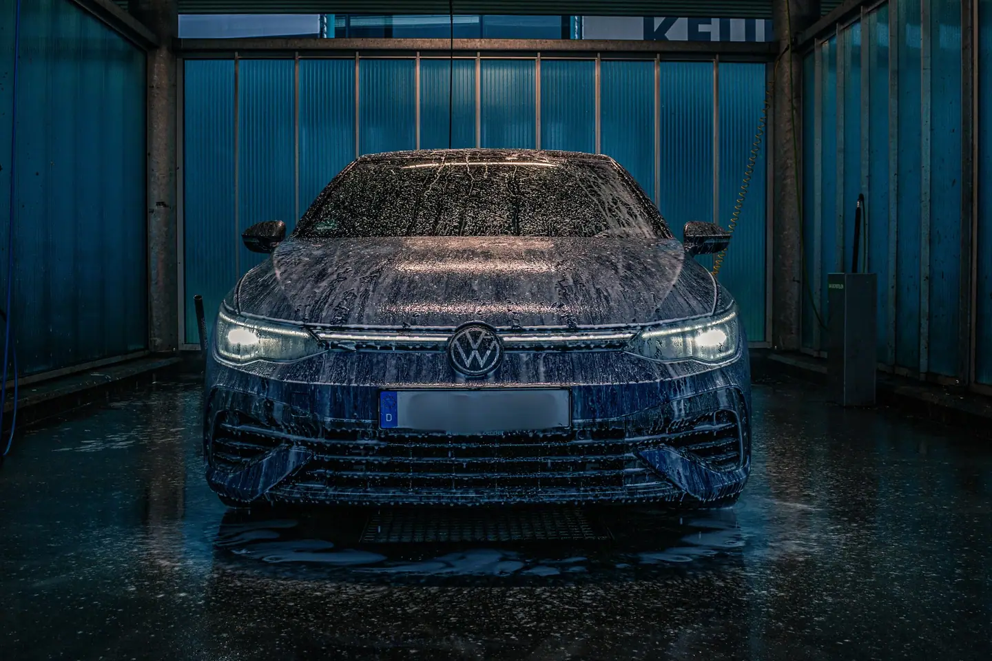 Volkswagen Golf R recht van voren, volledig bedekt met schuim in een donkere wasbox