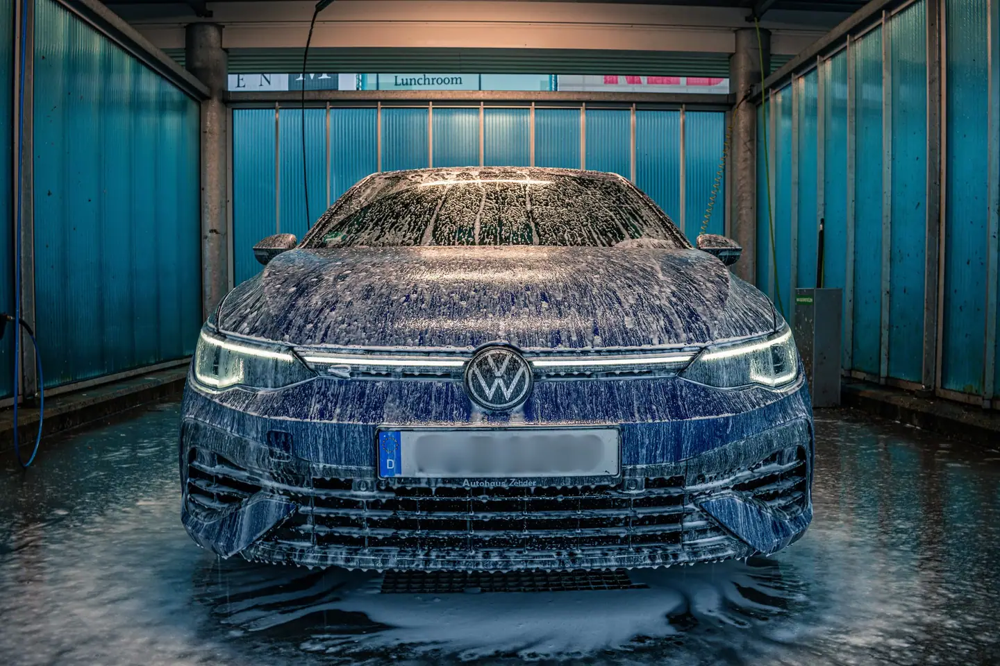 Volkswagen Golf R recht van voren onder een dikke laag schuim in een wasbox, met warm licht en turquoise wanden