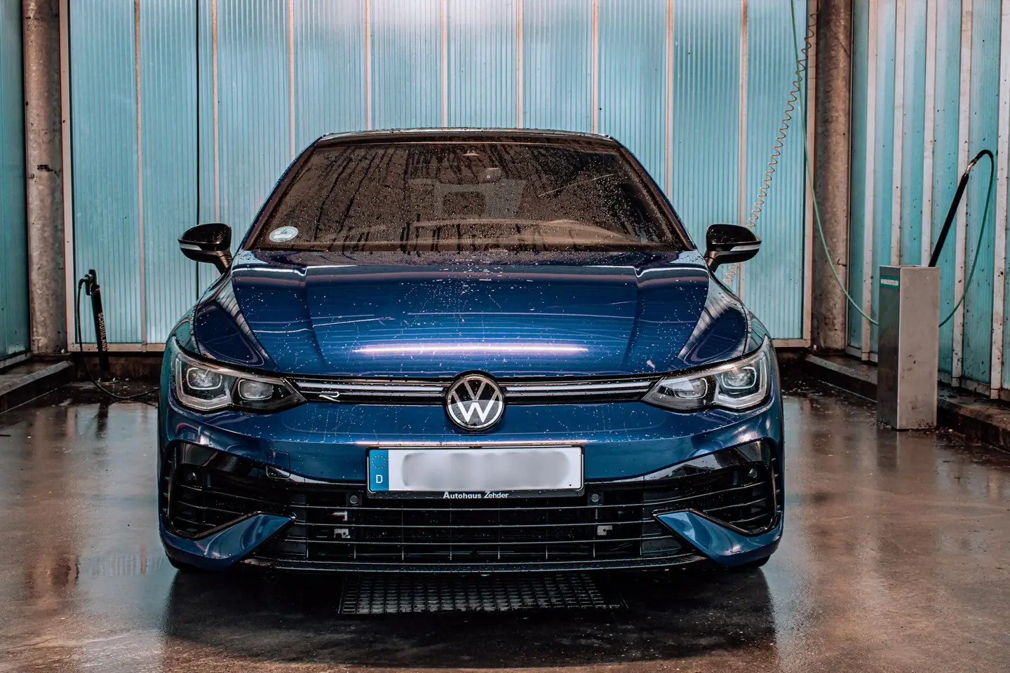 Schone, natte blauwe Volkswagen Golf R recht van voren in een wasbox met turquoise wanden