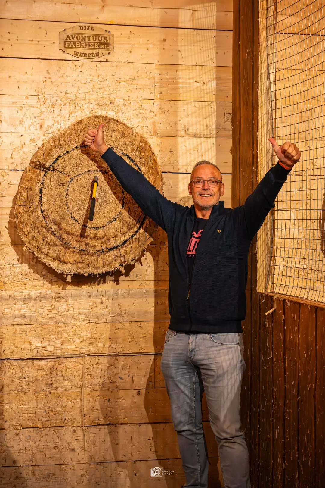 Een gast steekt beide duimen op naast de schijf waarin zijn bijl vastzit.
